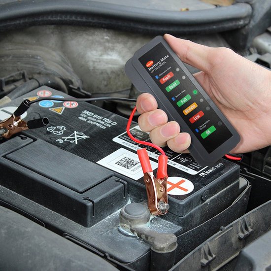 Hand met grijze accutester boven een autoaccu. De tester toont 'Middle' en de rode lampjes voor 'Low' en 'Fault' zijn aan.