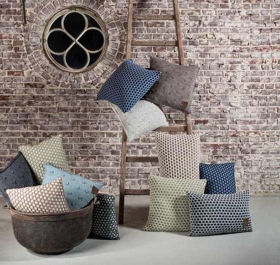 Collectie sierkussens in diverse kleuren en patronen, gestyled op een ladder voor een rustieke uitstraling.