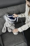 Vrouw met witte blouse strijkt een konijnenknuffel met een donkerblauwe Tefal stoomgenerator.