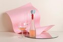 Grijze olifant wijnstopper op een fles, naast wijnglazen, met roze decoratie.