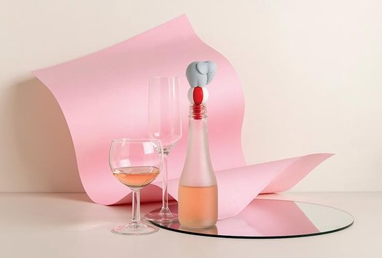 Grijze olifant wijnstopper op een fles, naast wijnglazen, met roze decoratie.