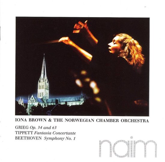Een vrouwelijke dirigent met golvend bruin haar, gericht op een orkest met baton in haar hand, met op de achtergrond een kathedraal.