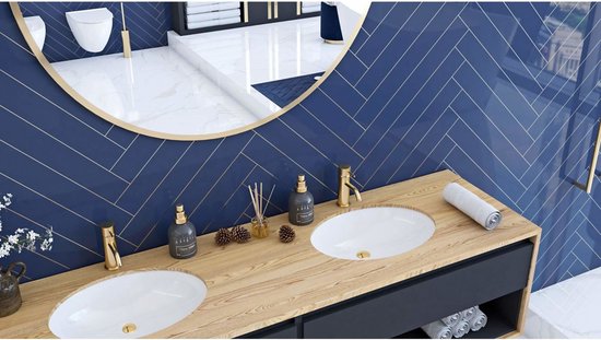 Miroir à bordure dorée reflétant une salle de bain avec lavabo double et carreaux bleu marine en chevrons.