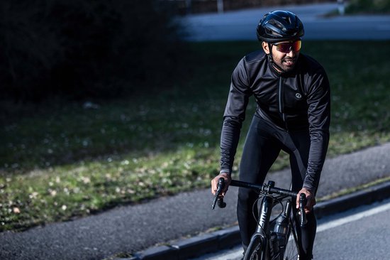 Man op fiets in zwart fietsjack, fietsbroek en helm, rijdt op een weg.
