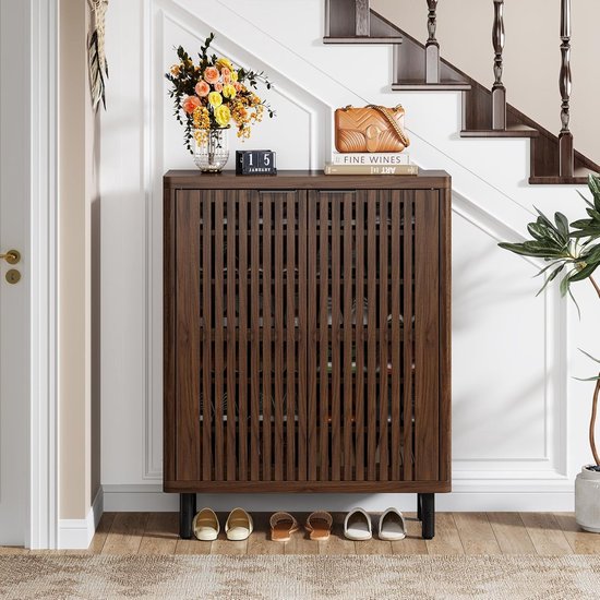 Meuble à chaussures couleur noyer foncé avec façade à lamelles et pieds noirs, avec un sac et des fleurs sur le dessus, à côté d'un escalier.