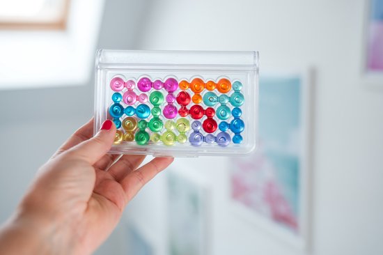 Hand houdt een gesloten speldoosje vol met gekleurde bubbels in verschillende vormen.