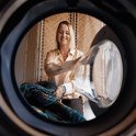 Vrolijke vrouw met blond haar, steekt een bontgekleurd dekbed in een wasmachine.