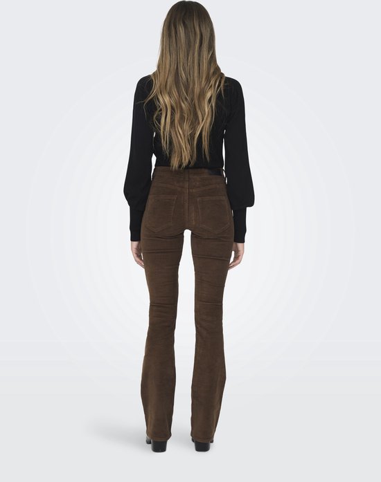 Vrouw met lang bruin haar, in zwarte coltrui en bruine corduroy flare broek.