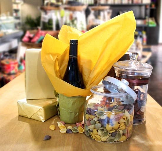 Gouden cadeaupakketten, rode wijnfles in groen papier, pot met gekleurde pasta en pot met bruine snoepjes.