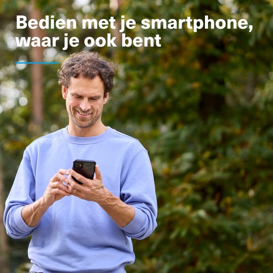 Man in blauwe trui lacht naar zijn smartphone, buiten met bomen op de achtergrond.