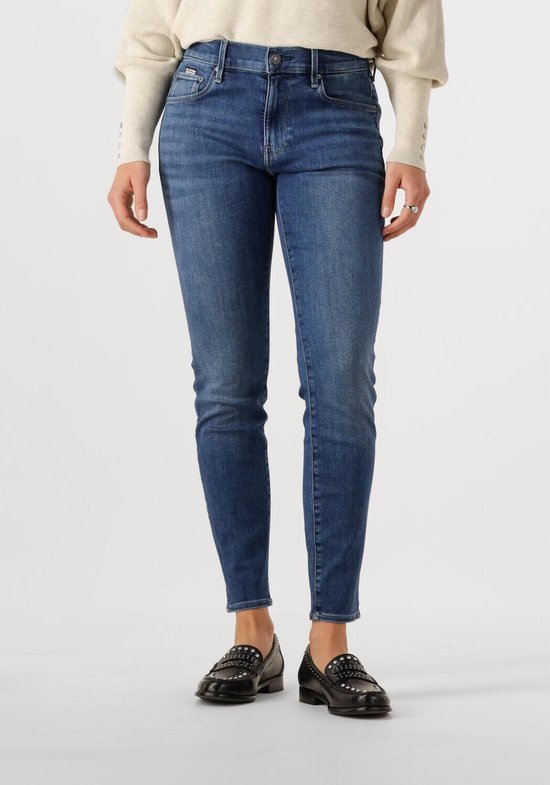 Dames skinny jeans in medium blue denim, gedragen met een beige trui en loafers.