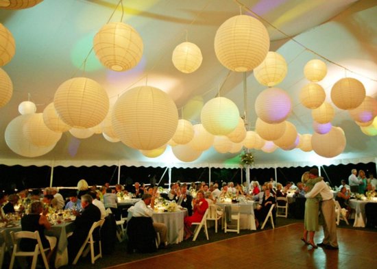 Feesttent met lichtgevende witte en gekleurde papieren lampionnen boven gasten.