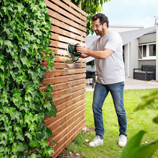 Man schuurt een houten schutting met een groene Bosch excenterschuurmachine.