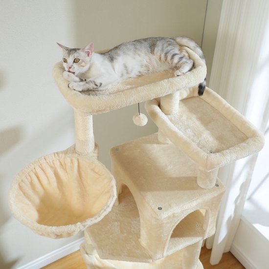 Gestreepte kat met witte poten, liggend op een beige platform van een kattentoren, bij een hangende bal.
