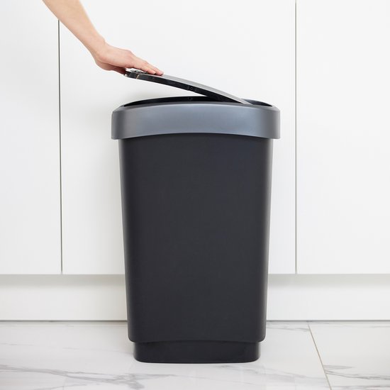 Hand opent grijze afvalbak met donkergrijs deksel in een witte keuken.