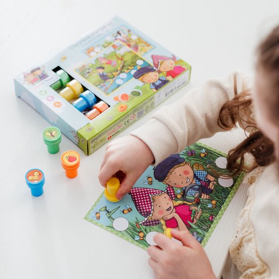 Een kind gebruikt een oranje stempel met een appelafbeelding op een kaart met Fien & Teun en bijen. De stempeldoos ligt ernaast.