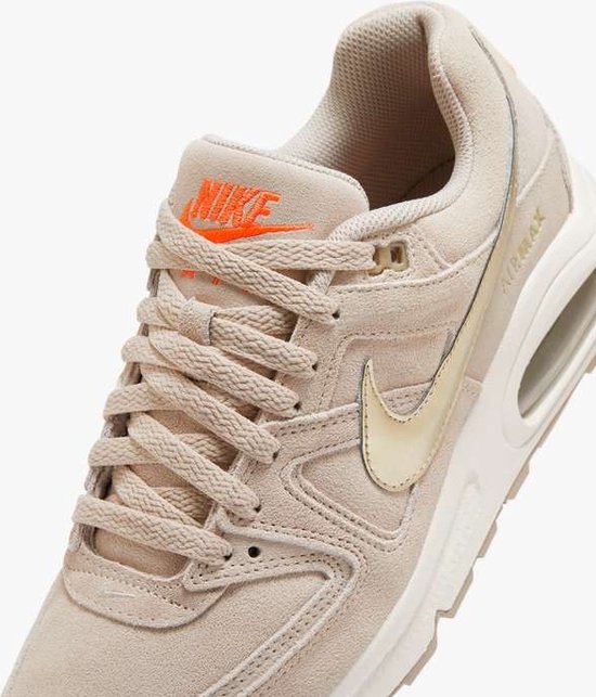 Close-up van beige Nike Air Max Command PRM sneaker met oranje Nike Air logo op de tong, beige veters, gouden swoosh en Air unit.