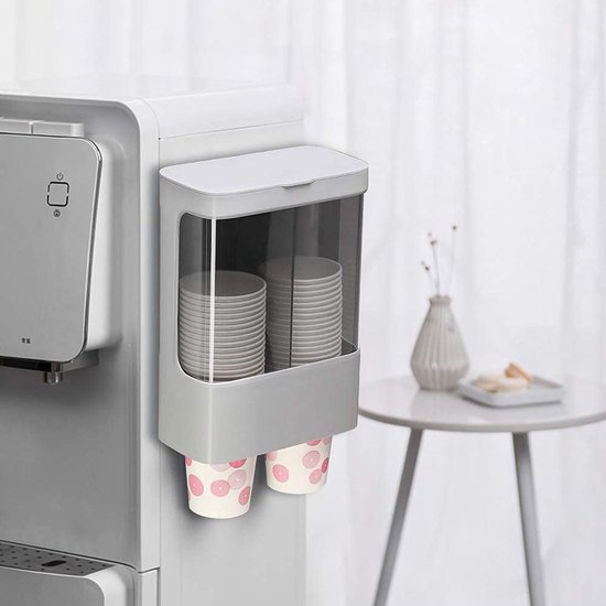 Grijze wandmontagedispenser met transparant voorvak, gevuld met witte bekers, hangend naast een waterdispenser.