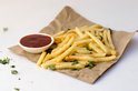 Goudbruine frietjes met platte peterselie en een bakje ketchup op bruin bakpapier.
