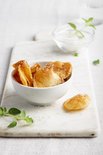 Goudbruine aardappelchips met zout in een witte kom op een marmeren plankje.