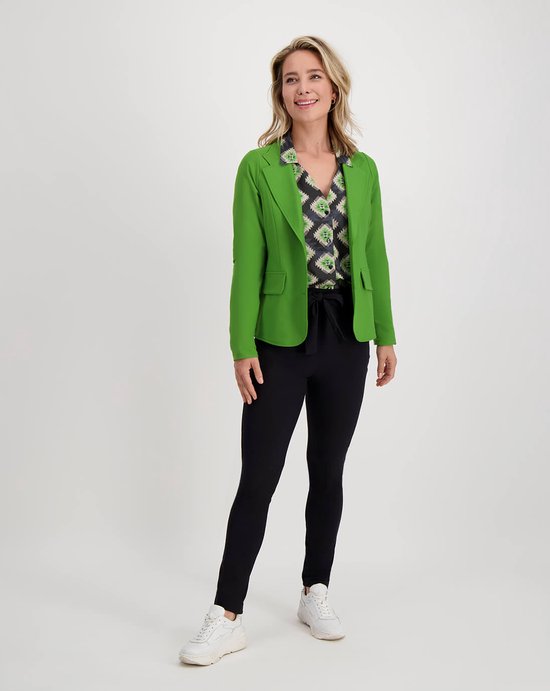 Model met zwarte slim fit broek, groen jasje en blouse met grafische print.
