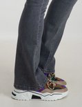 Onderste deel van benen in een grijze spijkerbroek met flared pijpen en kleurrijke sneakers.