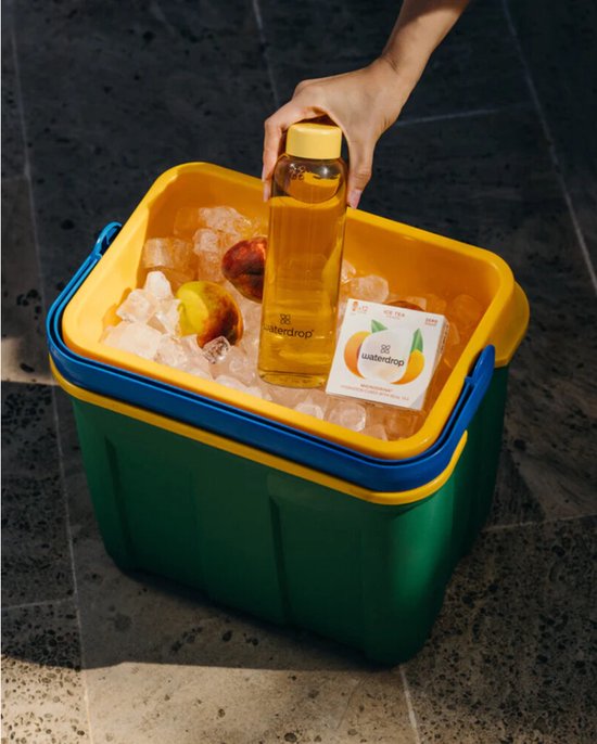 Hand plaatst een fles water in een koelbox met ijs, perziken en een waterdrop Ice Tea Peach doosje.