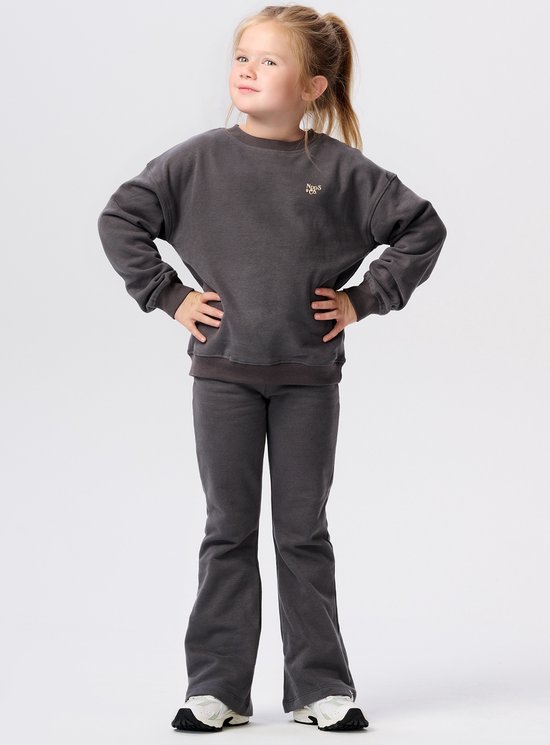 Meisje in donkergrijs joggingpak met ronde hals en wijduitlopende broekspijpen.
