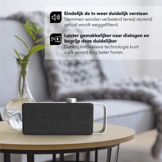 Zwarte luidspreker met zilveren handgreep op een houten tafel. Achtergrond van een woonkamer met bank. Tekst: "Eindelijk de tv weer duidelijk verstaan" en "Luister gemakkelijker naar dialogen".