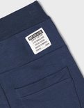 Detail van een donkerblauwe joggingbroek met een label met tekst en een achterzak.