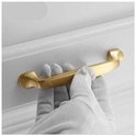 Een hand met een grijze handschoen bevestigt een matte gouden greep aan een witte kast.