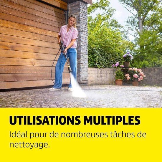 Vrouw gebruikt Karcher hogedrukreiniger op terras bij houten garagedeur, "Utilisations Multiples" voor diverse schoonmaaktaken.