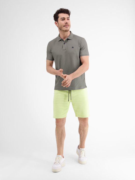 Man in donkergrijs poloshirt en lichtgroene korte broek, staat naar voren.