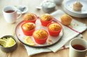 Zes citroenmuffins in rode siliconen vormpjes op een bord, met citroenschijfjes. Een kopje thee staat ernaast.