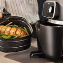 Een mand met een geroosterde kip en groene asperges wordt uit de Philips Airfryer Combi XXL gehaald.