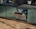 Inbouwvaatwasser met roestvrijstalen front, open deur met vaat, geïntegreerd in keuken met groene kasten.