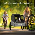 Man en kind fietsen met een hondenfietskar in een park. "Maak jouw gezinsuitjes compleet" staat in tekst.