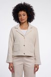 Femme aux cheveux bouclés portant une veste courte couleur crème à col revers, boutons dorés et poches à rabat.