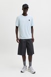 Man met donkere huid in lichtblauwe t-shirt, grijze korte broek en zwarte pet.