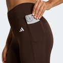 Vrouw stopt telefoon in zakje van donkerbruine legging met wit Adidas logo.