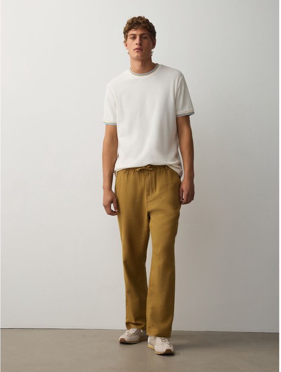 Model draagt een okergele broek van linnenmix met een witte t-shirt, rechte pasvorm, afgebeeld in staande positie.