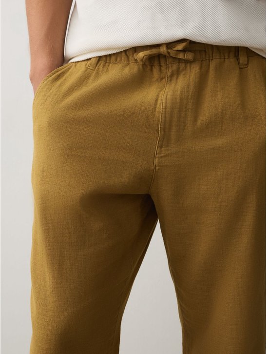 Close-up van de taille van een okergele broek van linnenmix met een elastische tailleband en trekkoord.