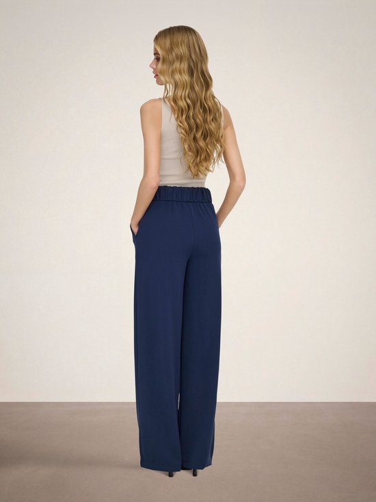 Model draagt donkerblauwe wijde broek met beige top.