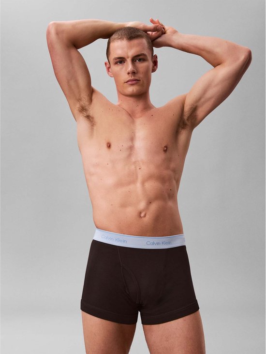 Man met bruine boxershorts met grijze Calvin Klein band, handen achter het hoofd.