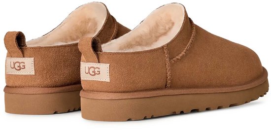 Achterkant van twee bruine suède UGG pantoffels met wollen voering en UGG-logo op de hielbandjes.