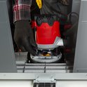 Een rode en grijze bovenfrees wordt door een hand met zwarte handschoen in de freestafel gemonteerd.