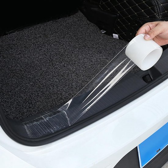 Hand brengt transparante beschermfolie aan op de instaplijst van een auto in de kofferbak.