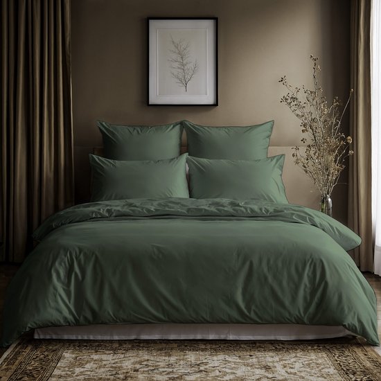Een compleet opgemaakt bed in donkergroene tinten, met kussens en een dekbed. Een tak in een vaas staat rechts.