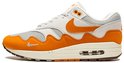 Zijzicht van een witte en oranje Nike Air Max 1 sneaker met beige zool en bruine accenten.