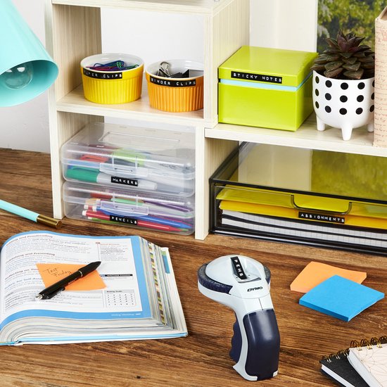 Dymo Omega labelmaker op een bureau met boeken, notitieblokken en gesorteerde pennen. Labelen van dossiers en bakjes.